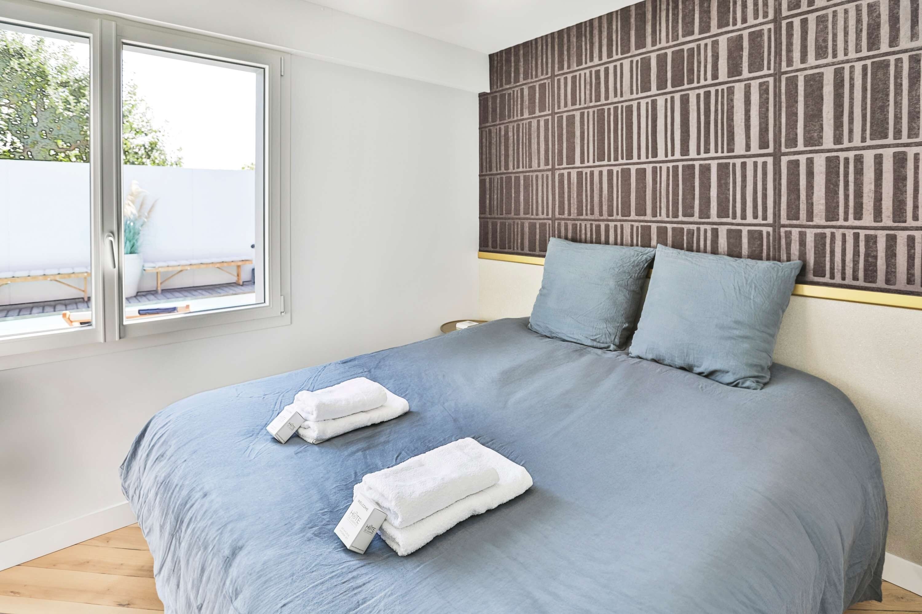 Un dormitorio con una cama grande, dos almohadas, un cabecero con motivos y una ventana con vistas a un balcón.