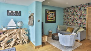A room with a blue wall, a wooden coffee table, a grey sofa, a white chair, a globe, a sailboat, and a floral-patterned wallpaper. - L'Océanide - dans une belle résidence avec piscine (Bretignolles-sur-Mer)
