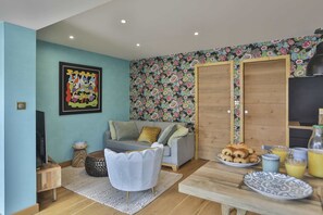 A living room with a sofa, coffee table, and breakfast setup with croissants and juice. - L'Océanide - dans une belle résidence avec piscine (Bretignolles-sur-Mer)