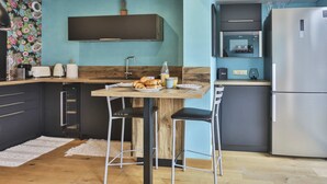 A modern kitchen with a wooden table, bar stools, a stainless steel refrigerator, and a microwave. - L'Océanide - dans une belle résidence avec piscine (Bretignolles-sur-Mer)