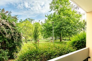 A balcony with a view of a lush garden, a street lamp, and a clear sky. - L’Écrin Vert d’Angers - À 100 m du tramway (Angers)