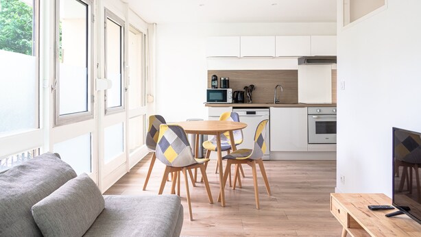 A modern kitchen with white cabinets, a dining table with chairs, and a TV on a wooden stand. - L’Écrin Vert d’Angers - À 100 m du tramway (Angers)