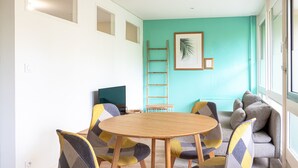 A modern room with a round wooden table, colorful chairs, a sofa, a ladder, and a framed picture on the teal wall. - L’Écrin Vert d’Angers - À 100 m du tramway (Angers)