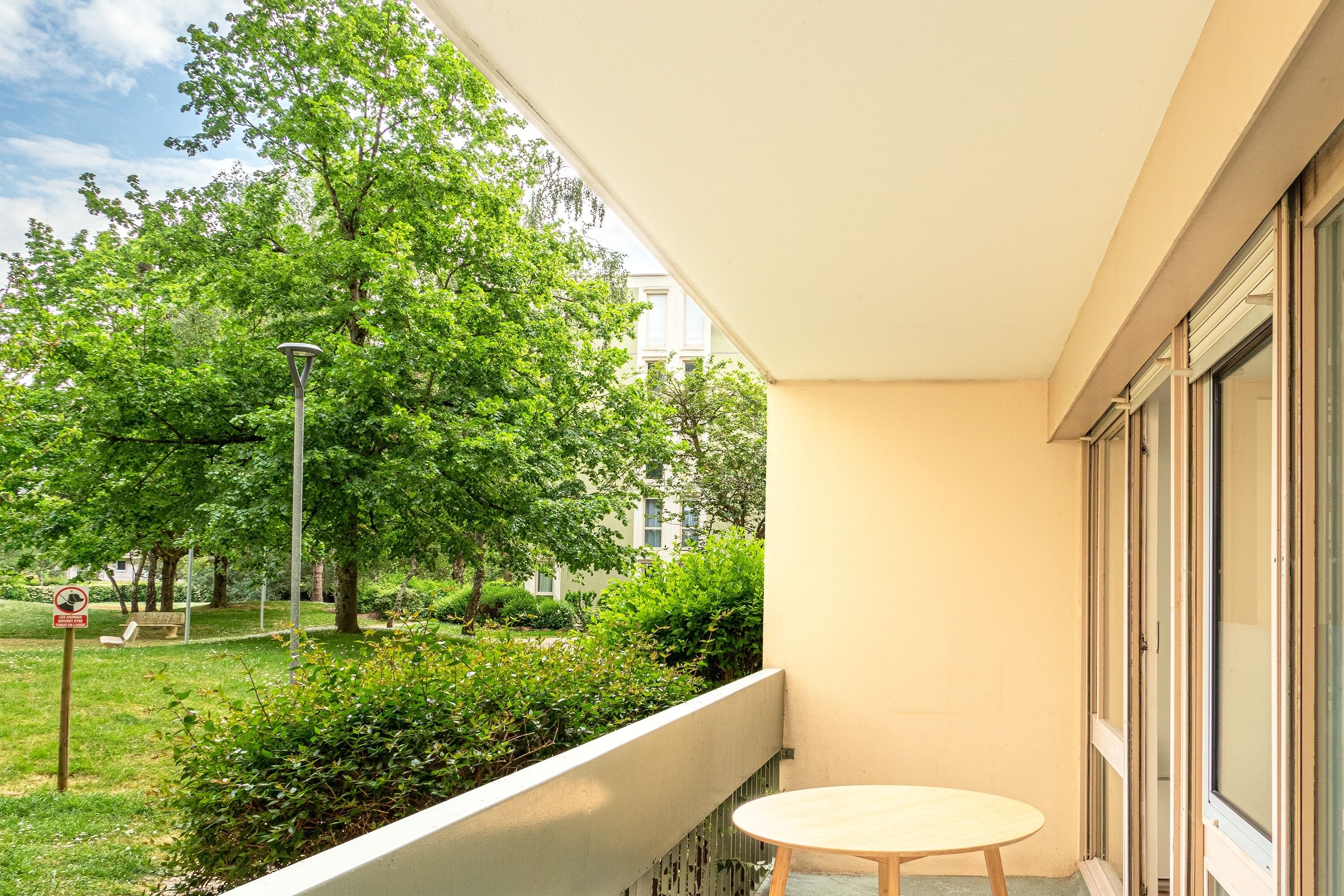 A balcony with a view of a park, a round table, and a building in the background.