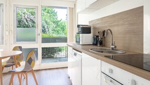 A modern kitchen with a built-in microwave, sink, and stove. There is a dining area with chairs and a table. - L’Écrin Vert d’Angers - À 100 m du tramway (Angers)