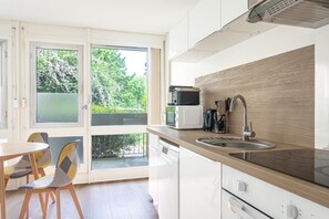 A modern kitchen with a built-in microwave, sink, and stove. There is a dining area with chairs and a table. - L’Écrin Vert d’Angers - À 100 m du tramway (Angers)