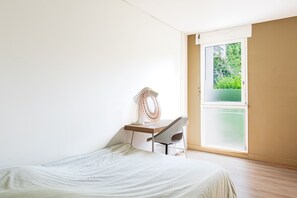 A bedroom with a bed, a desk with a chair, a window, and a view of greenery outside. - L’Écrin Vert d’Angers - À 100 m du tramway (Angers)