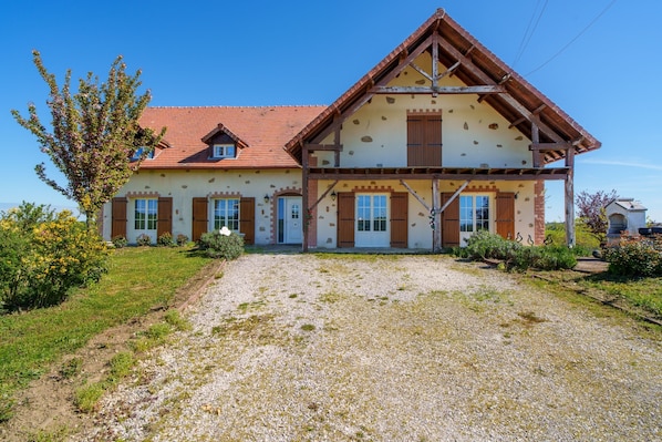 A two-story house with a red-tiled roof, wooden shutters, and a gravel driveway.