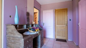 Un couloir avec une porte en bois, un vase bleu et un panier de fruits posé sur une commode.