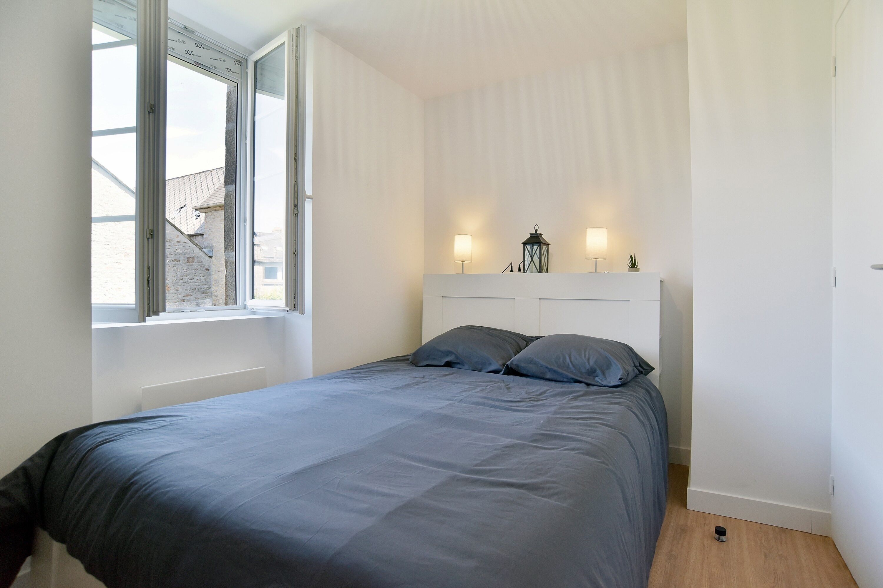 Une chambre à coucher avec un lit, une fenêtre et deux lampes fixées au mur.
