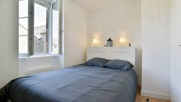 Une chambre à coucher avec un lit, une fenêtre et deux lampes fixées au mur.