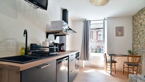 Una cucina moderna con lavastoviglie, fornello e televisore a schermo piatto. C'è una zona pranzo con tavolo e sedie, e vista sugli edifici attraverso una finestra.
