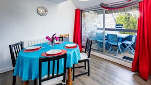 Un comedor con una mesa dispuesta para cuatro personas, un reloj en la pared y vistas al exterior a través de una puerta de cristal.