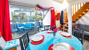 Un comedor con una mesa dispuesta para cuatro, una puerta de vidrio que da al exterior y una escalera al piso superior.