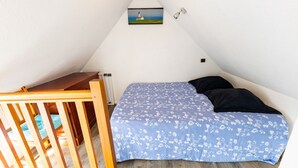 Un dormitorio con una cuna de madera, una cama con cubrecama floral, un cuadro en la pared y un techo inclinado.