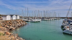 Eine Marina mit mehreren angestaubten Segelbooten, ein kleines Gebäude auf der linken Seite und ruhiges Wasser.