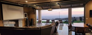 A modern living room with a large window, a sofa, and a dining area with chairs. - Rancho Del Sol.  An off-grid luxury retreat. (Poway)