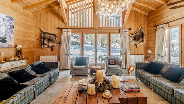 Ein Holzinnenraum mit hohen Decken, zwei Sofas, einem Couchtisch mit Kerzen und einem großen Fenster.