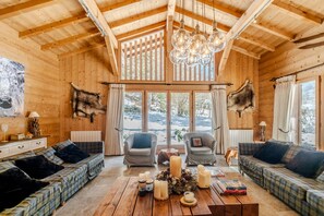 Un interior de madera con techo alto, dos sofás, una mesa baja con velas y un ventanal grande.