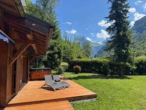 Terraza de madera con sillones de descanso, jacuzzi y vista a la montaña.