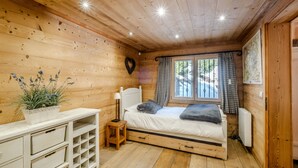 Ein Schlafzimmer in einer Holzhütte mit Bett, Nachttisch, Schminktisch und einem Fenster mit Vorhängen.