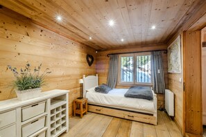 Un dormitorio de cabaña de madera con cama, mesita de noche, cómoda y ventana con cortinas.