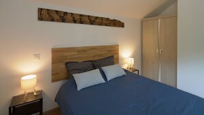 A bedroom with a wooden headboard, a bed with blue bedding, two bedside lamps, and a wardrobe. - La Sittelle - Appt pour 4 à 25 km de Nantes (Héric)