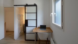 A room with a sliding door, a laptop on a wooden desk, a white chair, and a window. - La Sittelle - Appt pour 4 à 25 km de Nantes (Héric)