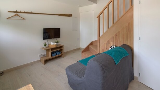 A modern living room with a sofa, TV, wooden staircase, and a wooden coat rack. - La Sittelle - Appt pour 4 à 25 km de Nantes (Héric)
