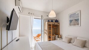 Een slaapkamer met een bed, een televisie, een kledingkast en uitzicht op zee.