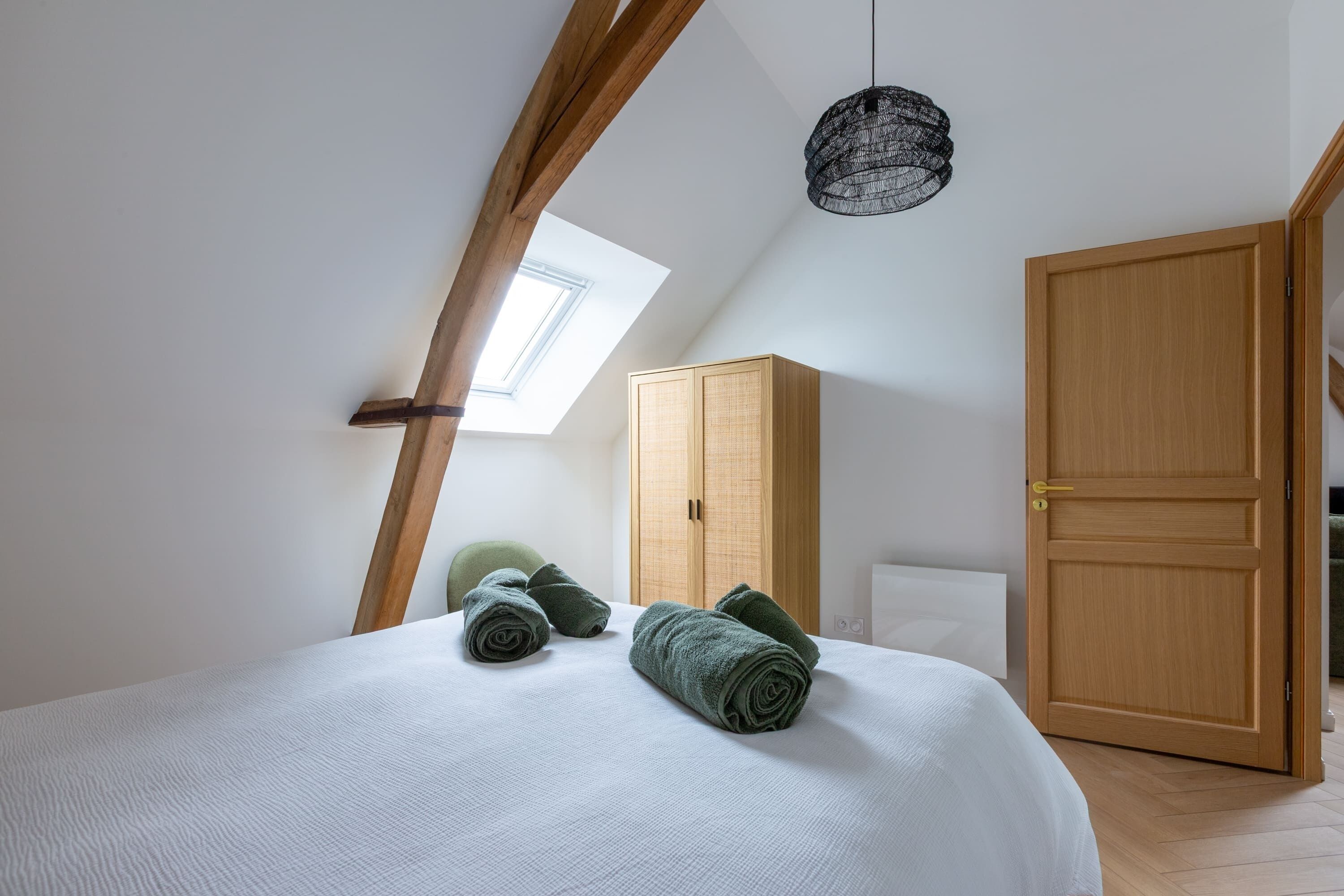 A bedroom with a bed, rolled towels, a wardrobe, and a skylight.