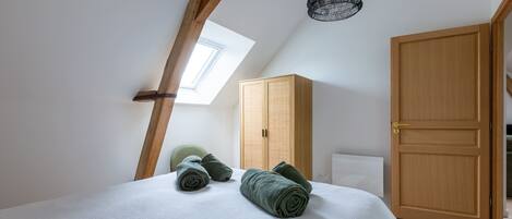 A bedroom with a bed, rolled towels, a wardrobe, and a skylight.