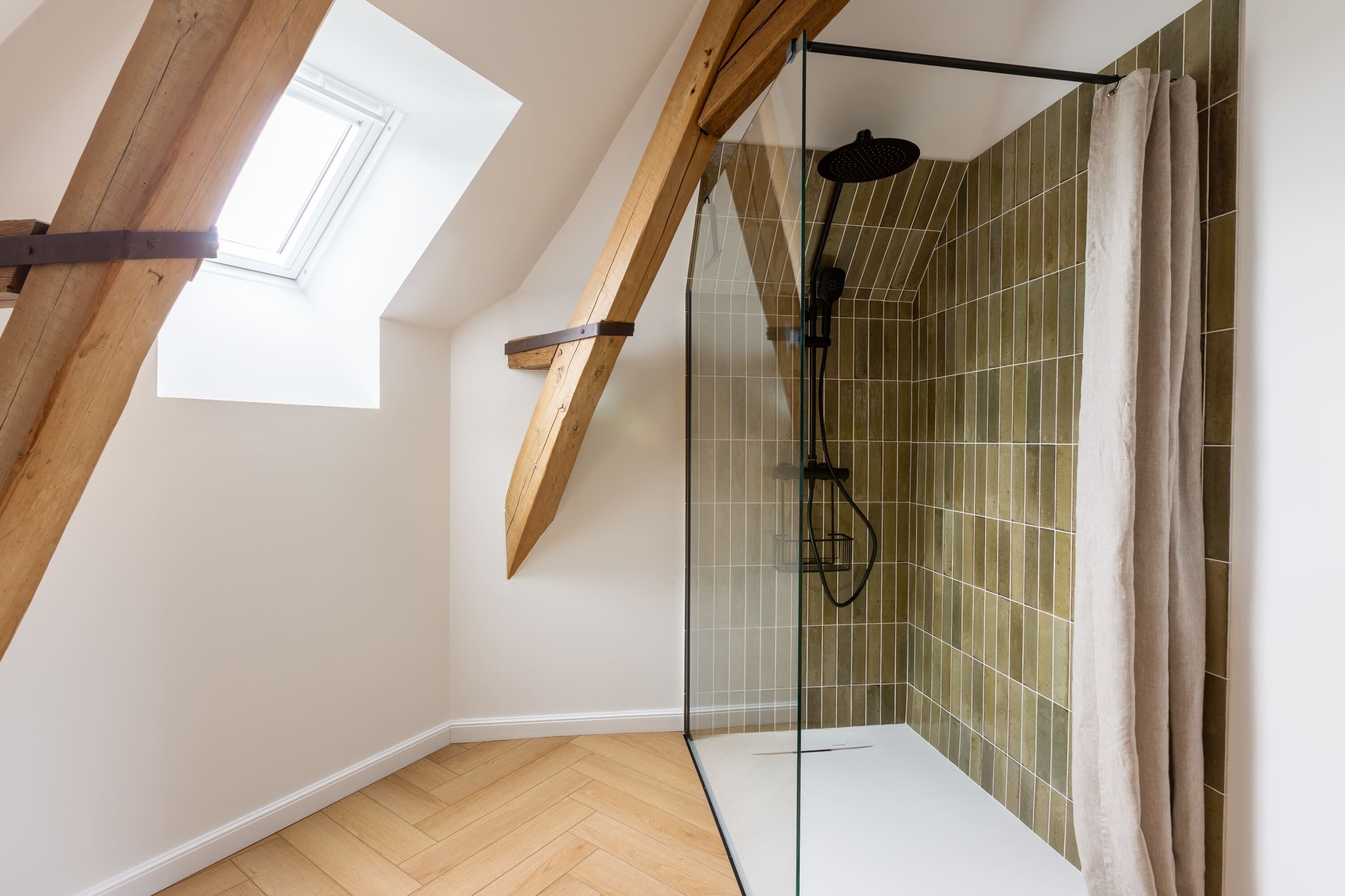 A modern shower with glass doors, a wooden ceiling, and a skylight.
