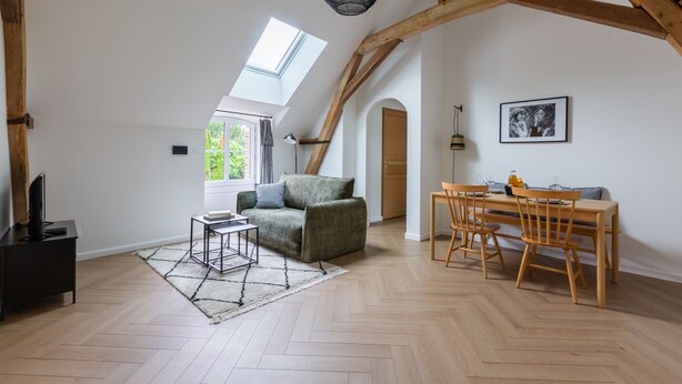 A spacious loft with a high ceiling, wooden beams, a dining area with a table and chairs, a sofa, a small side table, and a large skylight. - Louisa - Entre Nature et Loisirs (Saint-Calais)