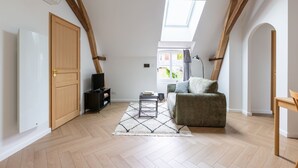 A room with a high ceiling, wooden beams, a skylight, a sofa, a small table, and a door. - Louisa - Entre Nature et Loisirs (Saint-Calais)