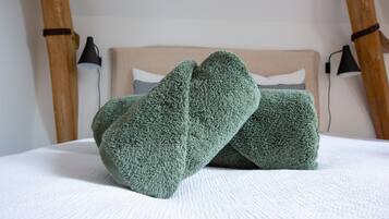 Un lit recouvert d’une couverture blanche à texture, deux serviettes vertes et une tête de lit recouverte d’un tissu de couleur claire.