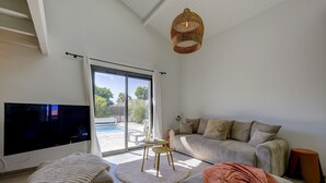 Ein Wohnzimmer mit Fernseher, Sofa, Hocker und einer Lampenschirm aus Weidwerk.