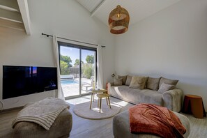 Ein Wohnzimmer mit Fernseher, Sofa, Hocker und einer Lampenschirm aus Weidwerk.