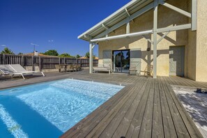 Eine Holzterrasse mit Pool, Sitzgelegenheiten im Freien und einer überdachten Veranda.