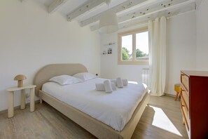 Ein Schlafzimmer mit Bett, Nachttisch, Lampe und einem Fenster mit Vorhängen.