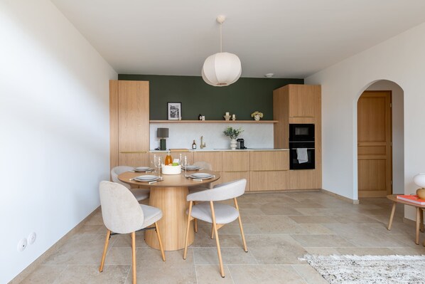 Une cuisine moderne avec des meubles en bois, une table à manger pour quatre personnes et un luminaire suspendu.