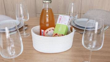 Une table à manger sur laquelle se trouve un panier en osier blanc contenant une bouteille et une boîte, entourée de verres à vin et d’assiettes vides.