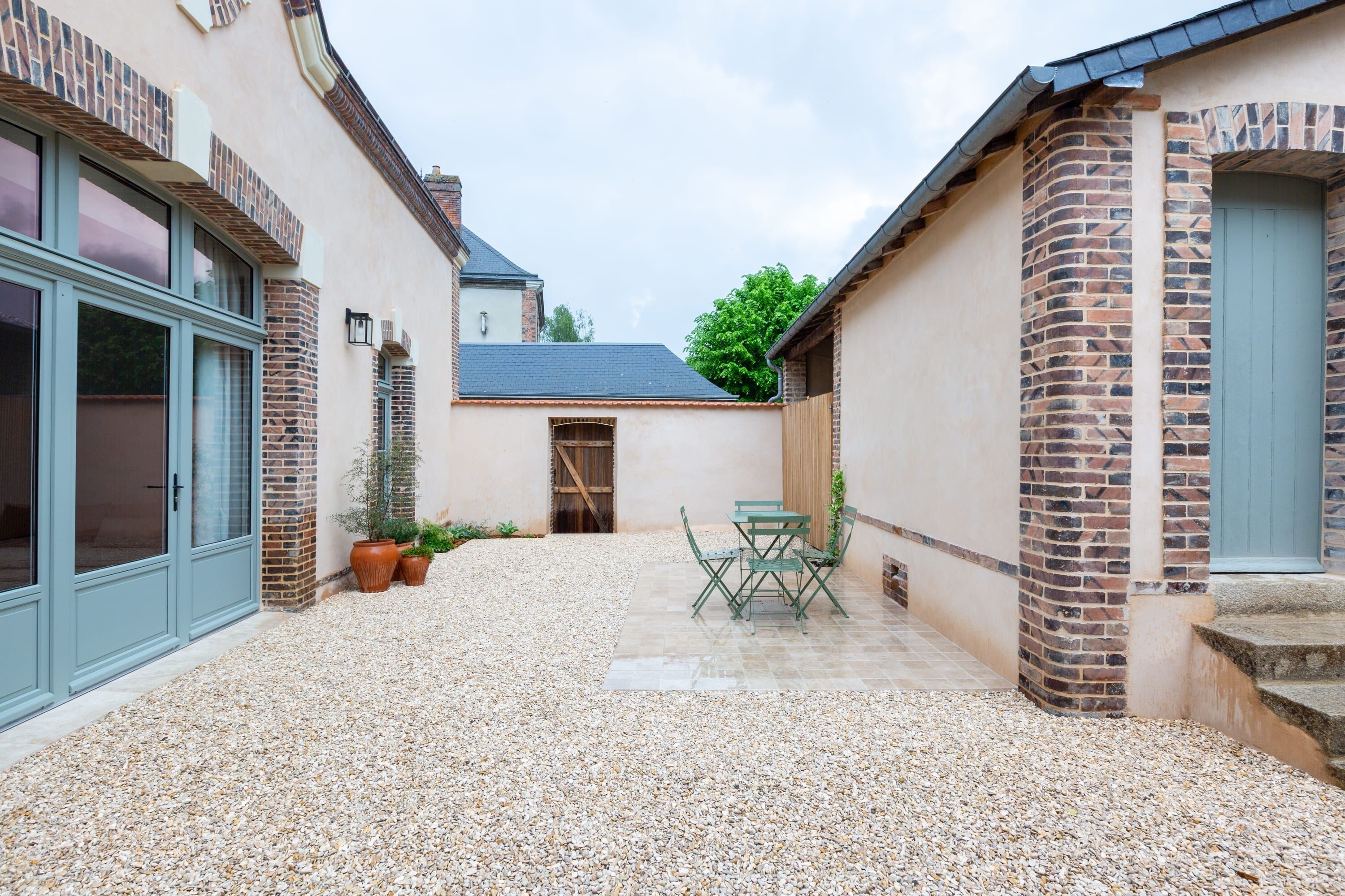 A courtyard with a gravel floor, a table with chairs, and potted plants.