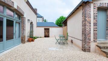 A courtyard with a gravel floor, a table with chairs, and potted plants.