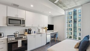 Une cuisine moderne équipée d’un four à micro-ondes, d’une cuisinière et d’un évier. On y trouve un lit donnant sur un immeuble, grâce à une grande fenêtre.