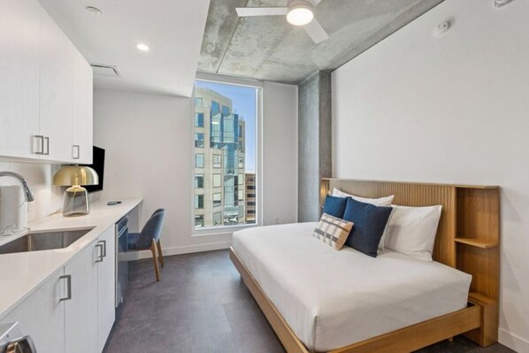 A modern bedroom with a bed, a desk, and a window with a city view. - Luxe Urban Escape in Phoenix | Full kitchen | Workspace & Resort Amenities (Maricopa County)