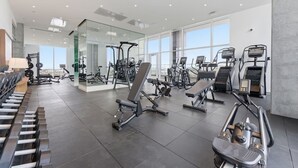 Une salle de sport moderne dotée de divers équipements d’entraînement, de grandes fenêtres et d’un aménagement propre et spacieux.