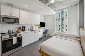 A modern hotel room with a kitchenette, a bed, a desk, and a window with a city view. - Luxe Urban Escape in Phoenix | Full kitchen | Workspace & Resort Amenities (Maricopa County)