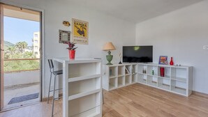 A modern living room with a TV, a sofa, a coffee table, and a balcony door. - L'Ecrin d'Hyères - Appt à 10 min de la plage (Hyères)