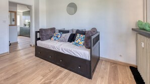 A modern bedroom with a dark wooden bed, a round mirror on the wall, and a view into the adjacent kitchen. - L'Ecrin d'Hyères - Appt à 10 min de la plage (Hyères)